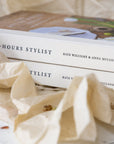 Two books titled 'Full-Hours Stylist' by Kate Williams & Anna McLeod on a marble surface with flowers.