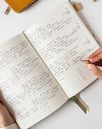Person writing in a notebook with a pen on a white surface