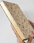 Hand holding a notebook with a floral pattern on a light gray background