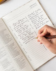 Hand writing in a notebook with a pen on a white surface