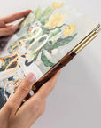 Hand holding a decorative pen over a notebook with floral design