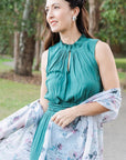 Woman in a teal dress with a floral scarf in a park setting