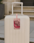 Beige suitcase with a pink floral luggage tag on a pavement.