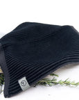 Black knit beanie with a brand tag on a white background with greenery