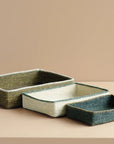 Set of three rectangular woven trays on a beige surface with a beige background