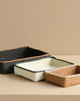 Three woven trays in black, white, and brown on a beige surface with a beige background