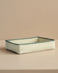 Rectangular woven basket with green rim on a beige background