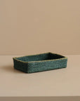 Green woven rectangular tray on a beige surface with a beige background