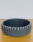 Gray felted bowl with white stitching on a wooden surface
