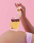 Hand applying perfume to a person's back against a pink background