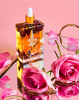 Glass dropper bottle with floral design on a pink surface with pink roses and petals.