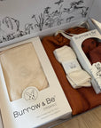 Baby clothing and accessories in a 'Bunrow & Be' box on a wooden surface