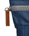 Close-up of a blue jacket zipper with a brown leather pull tab on a white background