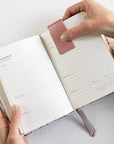 Person holding an open planner with a pink leather cover on a light gray background