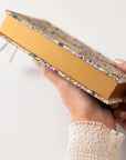 Hand holding a yellow notebook with a patterned cover on a white background