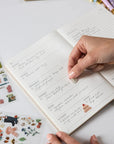 Handwritten notes in a notebook with decorative stickers and pens on a light surface