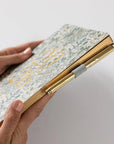 Hand holding a floral notebook with a gold edge on a light gray background
