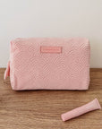 Pink textured pouch with a brand logo on a wooden surface