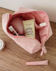 Pink toiletry bag with cosmetic items on a wooden surface