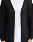 Person wearing a black open-knit cardigan over a white outfit on a light gray background