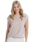 Woman wearing a beige top and white pants against a plain background