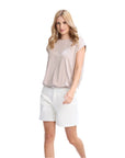 Woman wearing a beige sleeveless top and white shorts on a white background