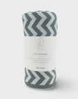 A rolled-up gray and white chevron-patterned travel towel with a white paper label wrapped around it, photographed on a light gray background.