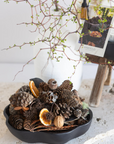 Decorative arrangement with pinecones, dried oranges, and branches on a white surface.