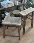 Two rustic wooden stools on a wooden floor with a store or home decor setting in the background.