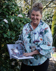 Woman holding a photo album outdoors with greenery in the background
