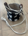 Black and white checkered bag with a long strap on a wooden floor