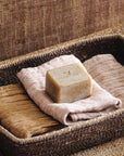 Bar of soap on a towel in a woven basket against a textured brown background