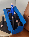 Blue hair styling tool case with hairbrushes and curling irons on a brown couch.
