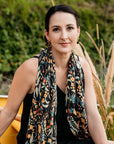 Woman wearing a patterned scarf sitting outdoors with greenery in the background