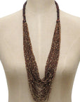 A long multi-strand statement necklace made of dark brown and bronze metallic beads, displayed on a beige mannequin torso against a white background.