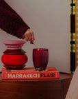 Person lighting a red candle on a book titled 'Marrakech Flair' with a decorative background.