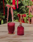 Red glass candle and diffuser set on a table with a Christmas tree in the background.