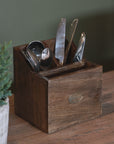 Wooden utensil holder with cutlery on a wooden surface with a green plant in the background