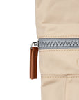 Close-up of a beige bag with a zipper and brown pull tab on a white background