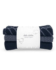 A three-pack of folded knit dish cloths in navy, charcoal gray, and black, wrapped in a white paper band labeled 'dish cloths variety 3 pack'.