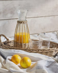 Carafe of orange juice on a woven tray with glasses and lemons on a white cloth against a wooden background