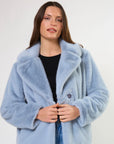 Woman wearing a light blue faux fur coat on a white background