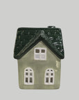 A small decorative house-shaped ceramic container or ornament with a dark green textured roof and a light sage green body, shown against a plain light gray background.