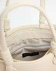 Close-up of a cream-colored handbag with a visible brand label on a light gray background