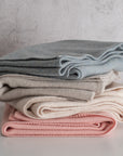 Stack of folded blankets in blue, beige, and pink on a light surface with a neutral background