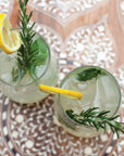 Two glasses of cocktails with lemon slices and rosemary on a patterned surface