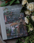 Book titled 'Floral Abundance' surrounded by flowers and greenery on a wooden surface
