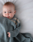 Baby wrapped in a gray blanket on a white surface