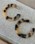Pair of tortoiseshell hoop earrings on a textured surface