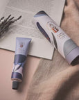 Two tubes of hand cream on a textured surface with a book and lavender.